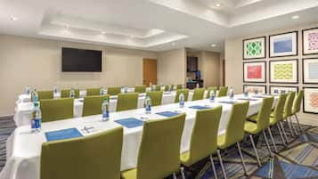 A conference room with tables, chairs, water bottles, and a TV screen.