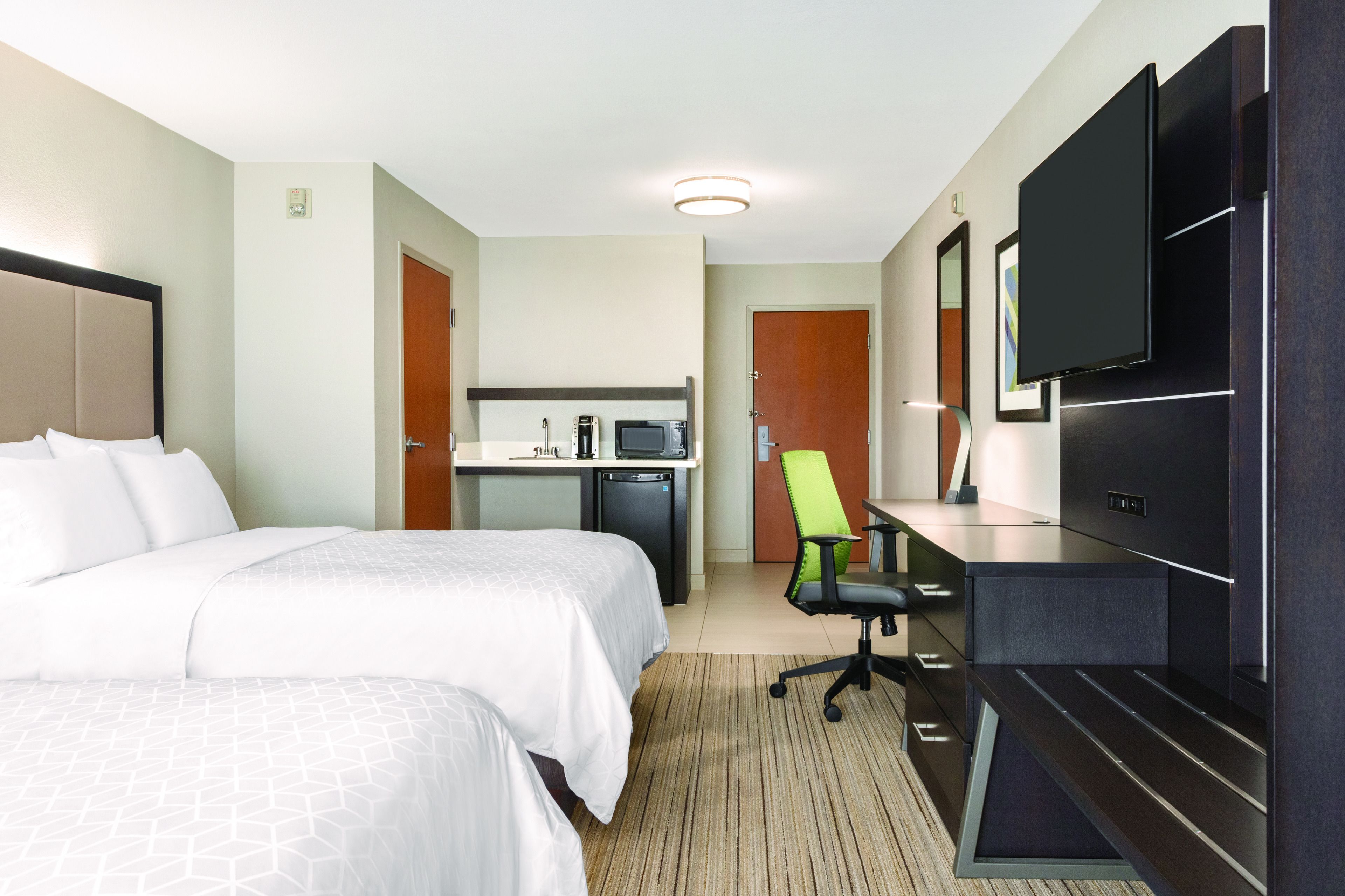 Quarto de hotel com duas camas, uma mesa, televisão e cozinha compacta.