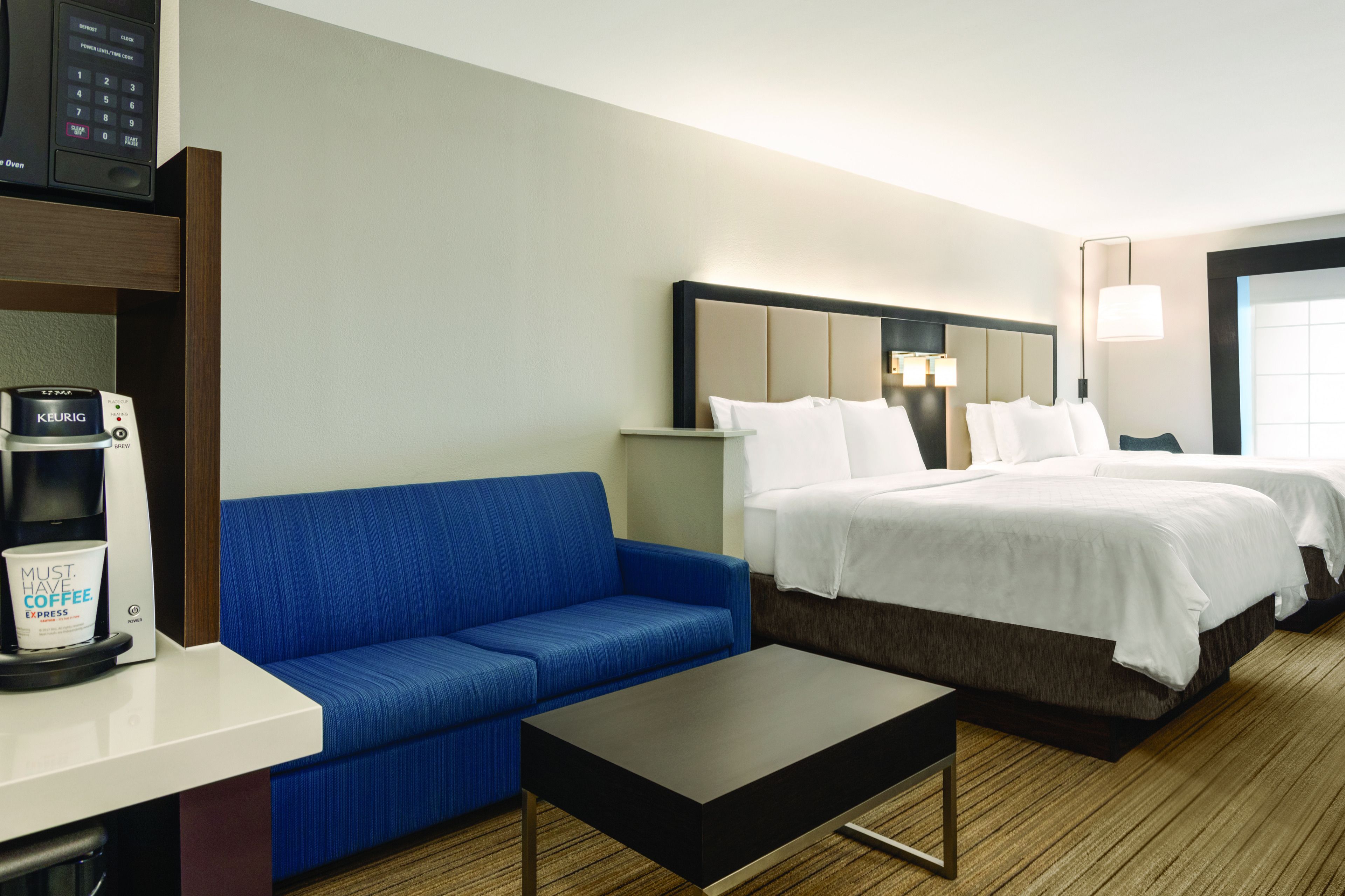 Une chambre d’hôtel avec un canapé bleu, un lit avec une literie blanche, une machine à café et une table de chevet.