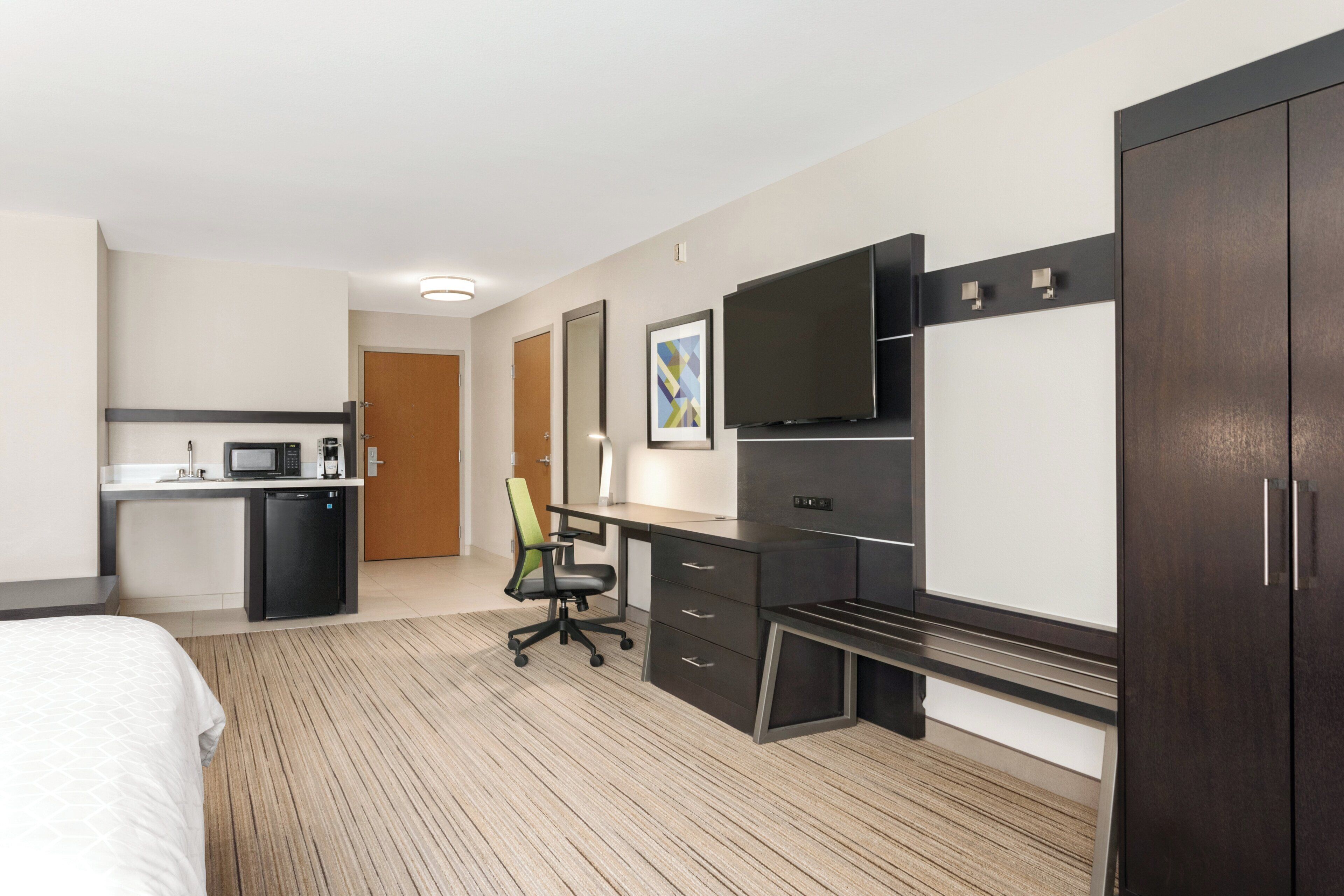 A hotel room with a bed, a desk with a chair, a television, and a wardrobe.