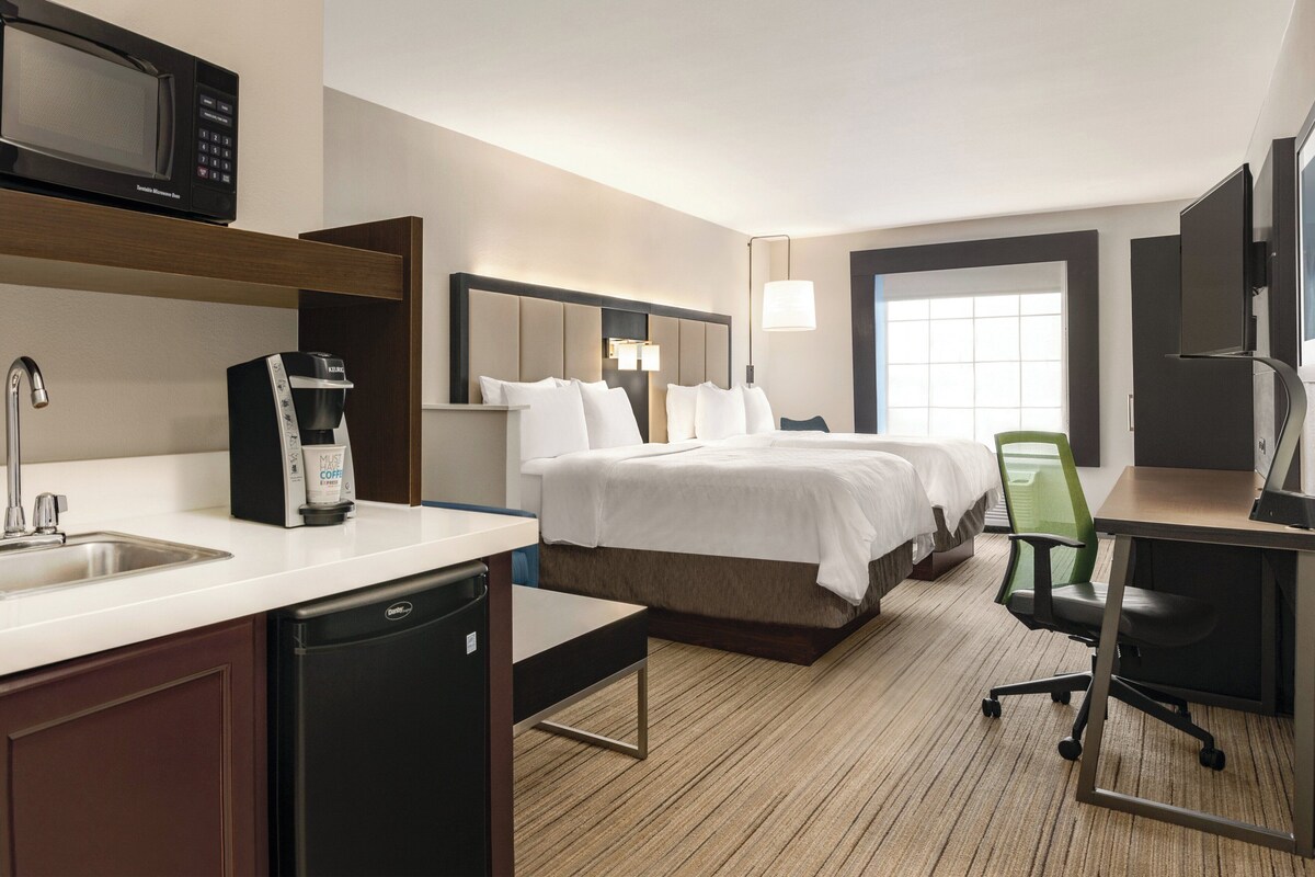 Ein Hotelzimmer mit Bett, Schreibtisch, Stuhl, Mikrowelle, Kaffeemaschine und Waschbecken.
