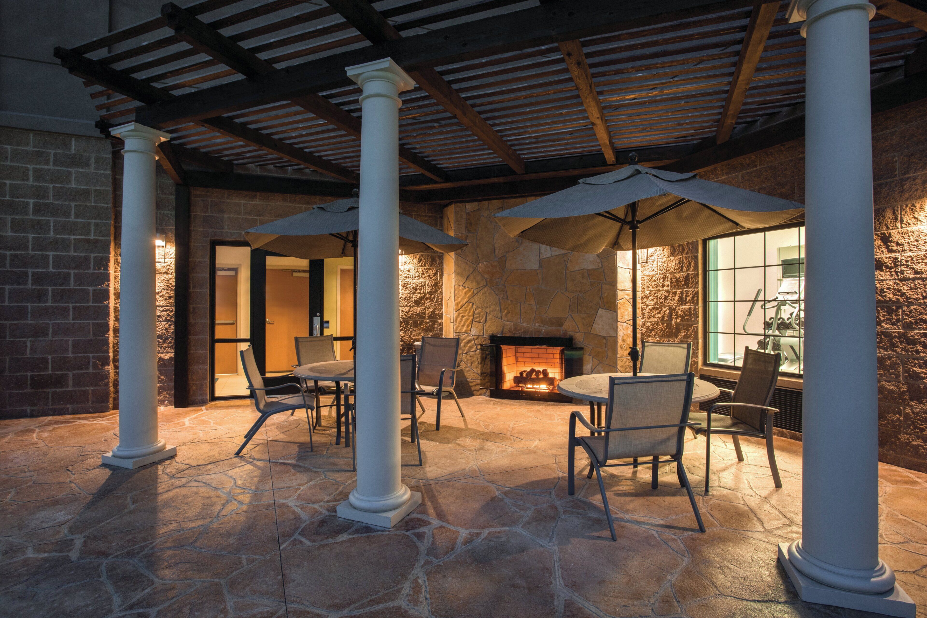 A stone-floored patio with outdoor seating, a fireplace, and a covered area with columns.