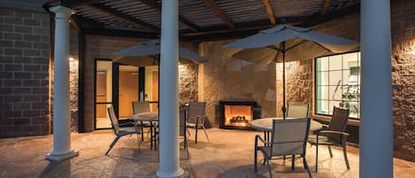 A stone-floored patio with outdoor seating, a fireplace, and a covered area with columns.