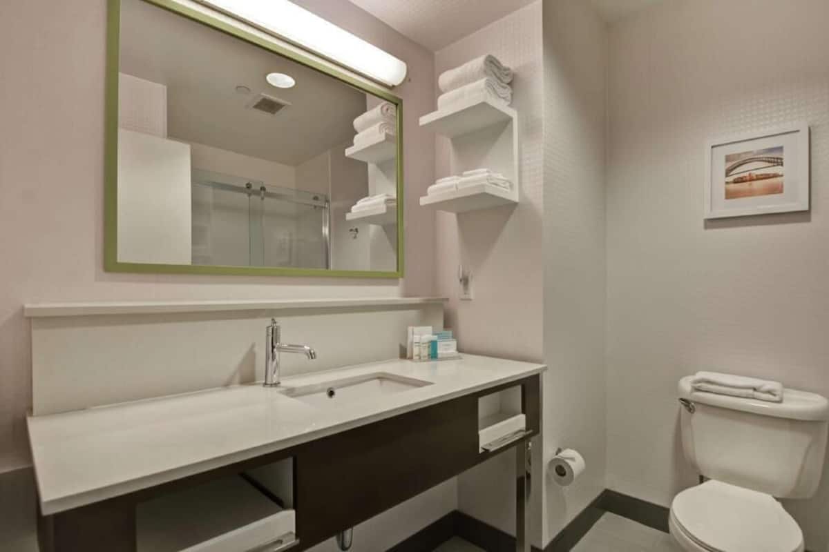 Un baño con lavamanos, espejo, toalleros y retrete.