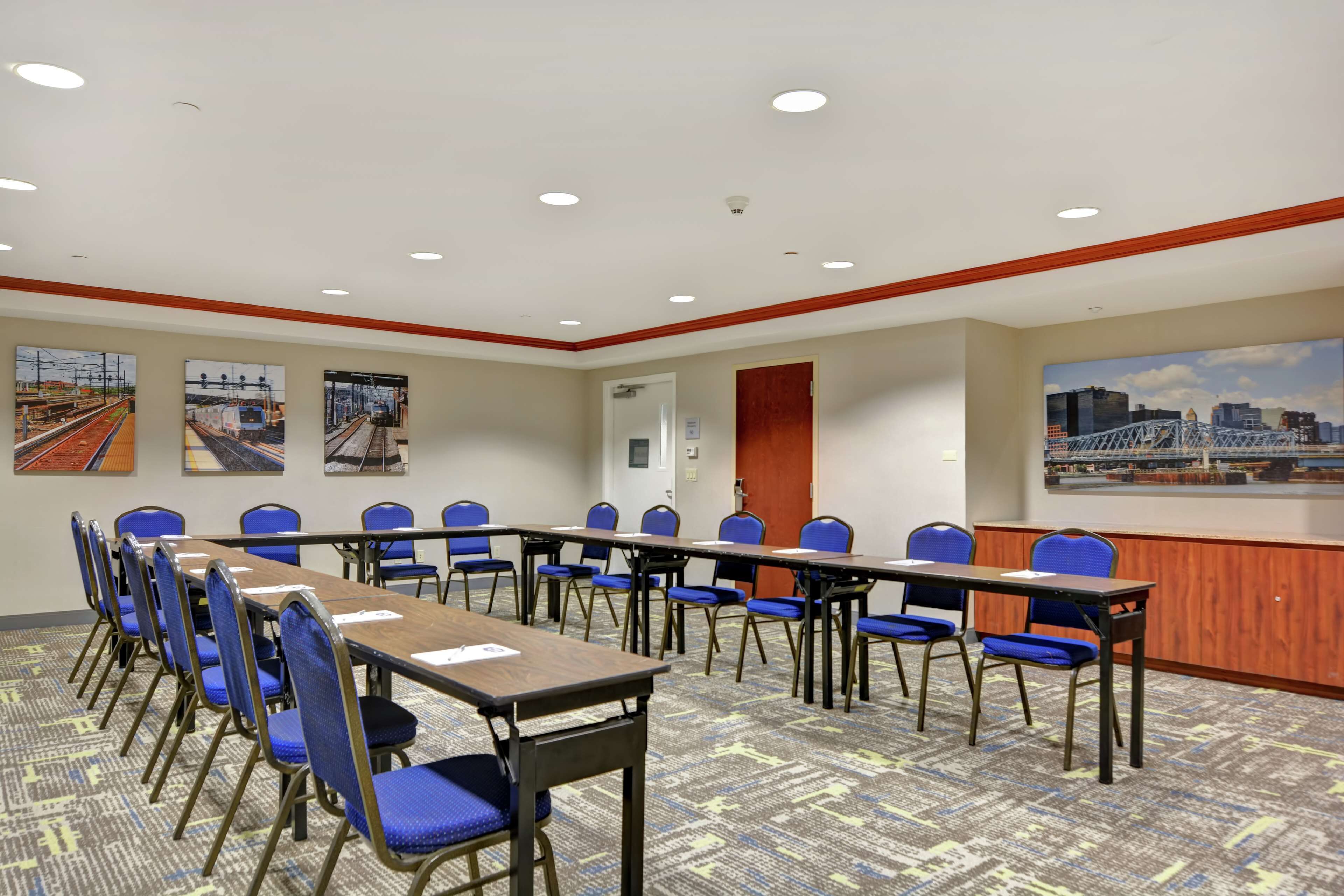 A conference room with a long table and blue chairs, decorated with cityscape paintings.
