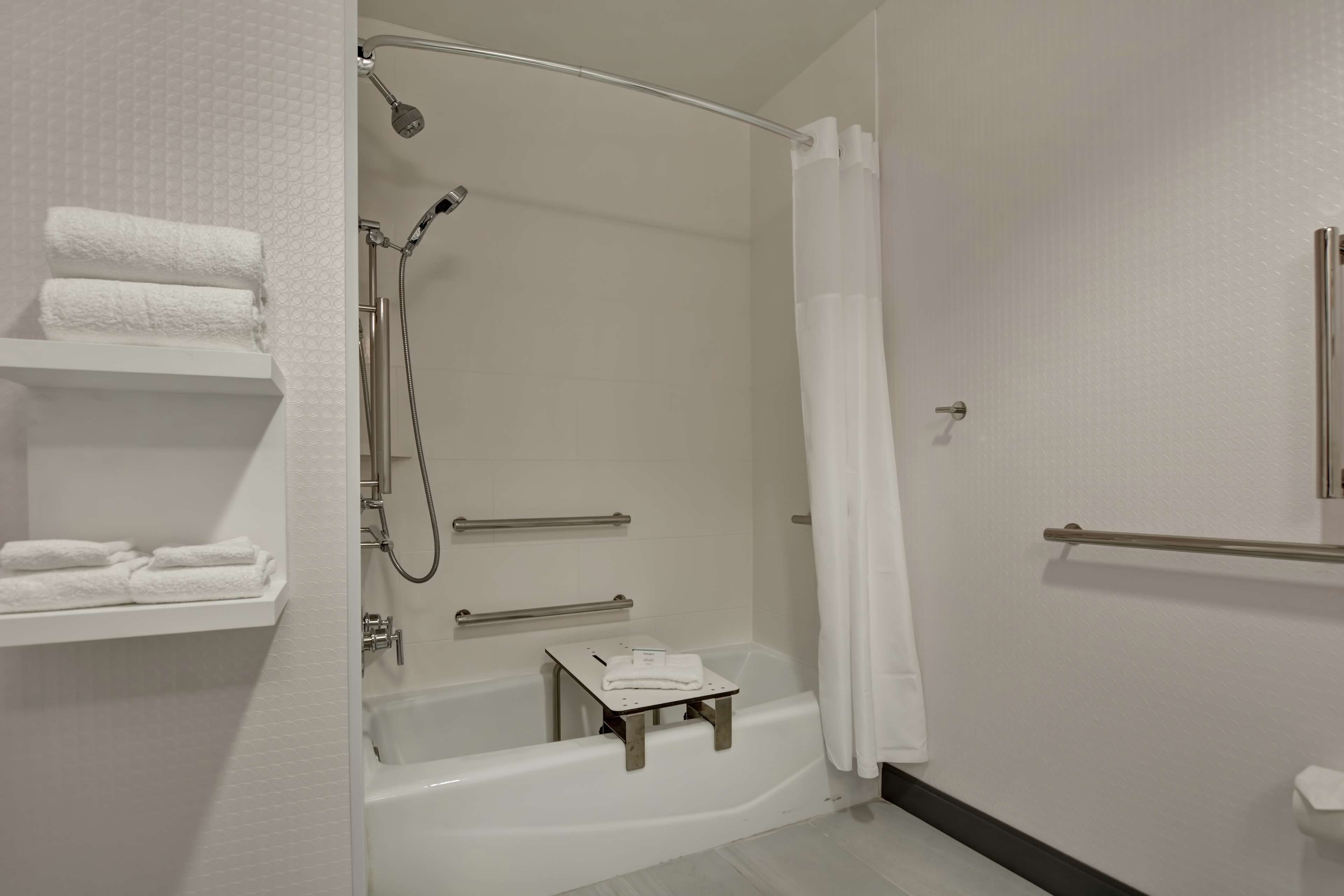 Un baño moderno con ducha acristalada, bañera blanca y un pequeño taburete de madera.