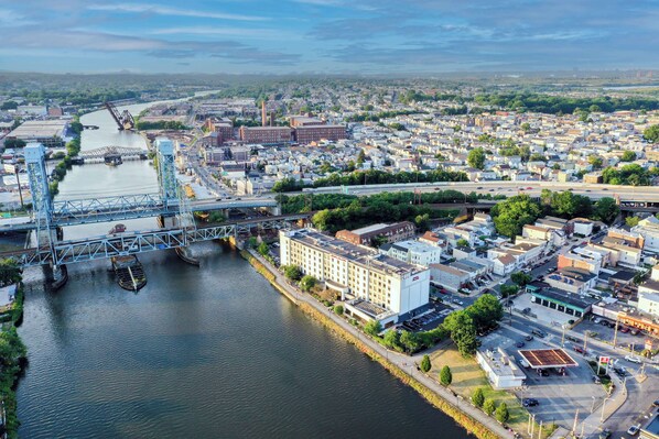 A river with a bridge, a large white building with multiple floors, and a parking lot with cars.