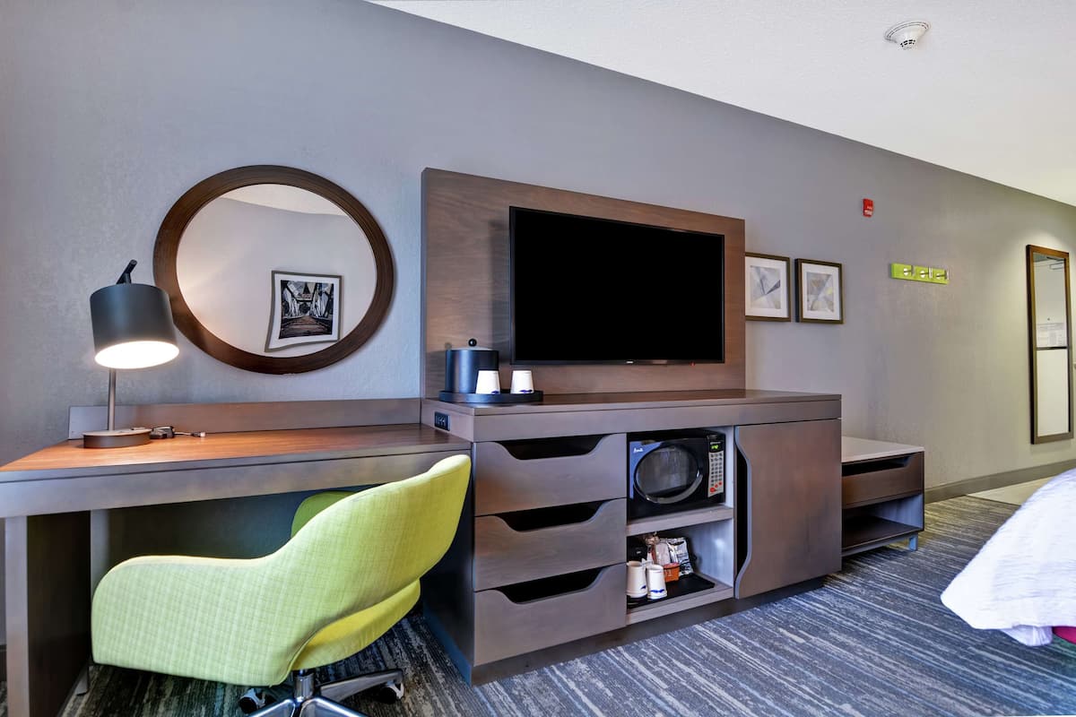 Una habitación de hotel con escritorio, silla, televisión, microondas y cama.