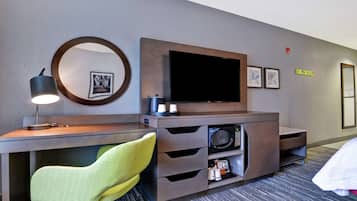 A hotel room with a desk, a chair, a television, a microwave, and a bed.