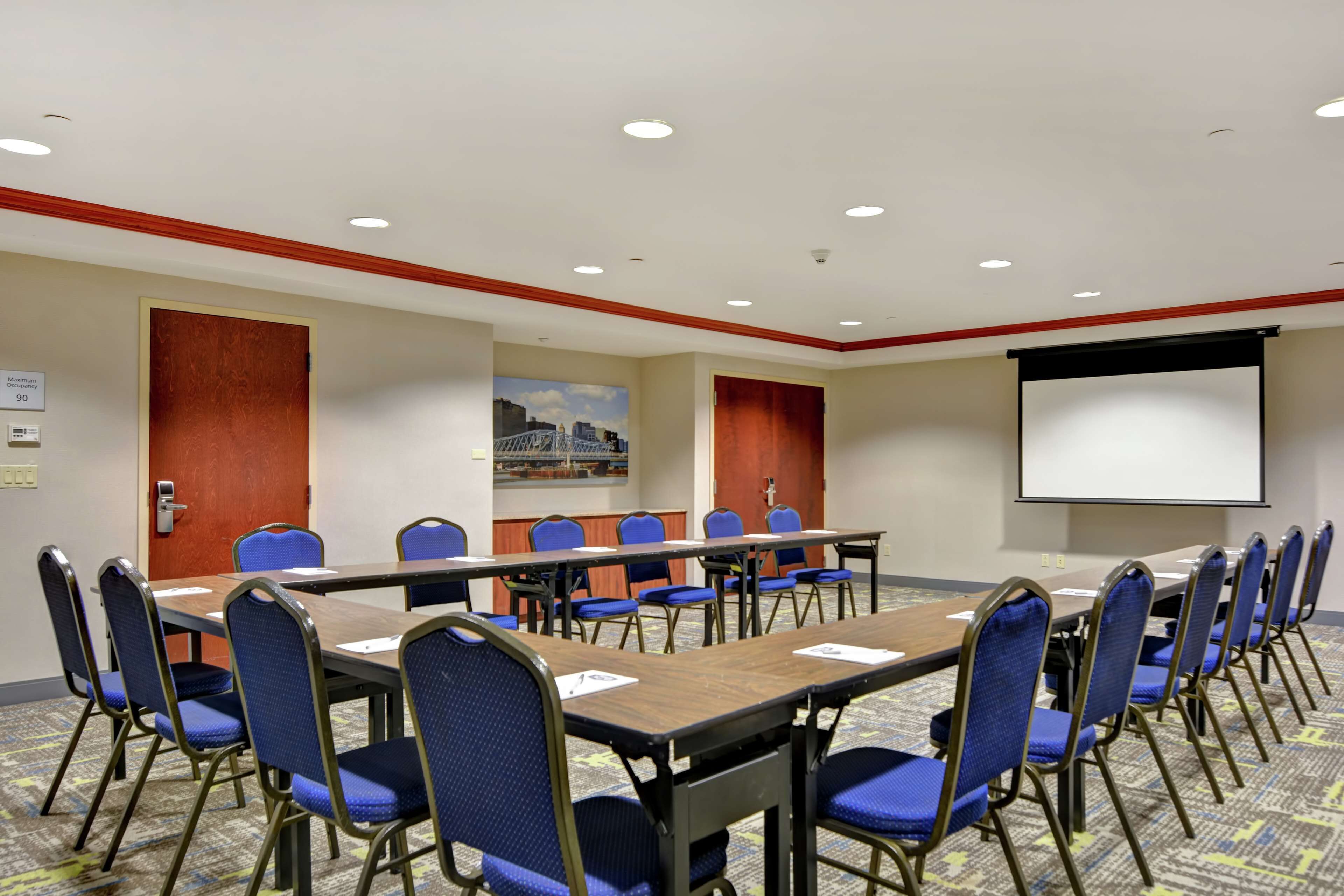 A conference room with a long table, blue chairs, a projector screen, and a carpeted floor.