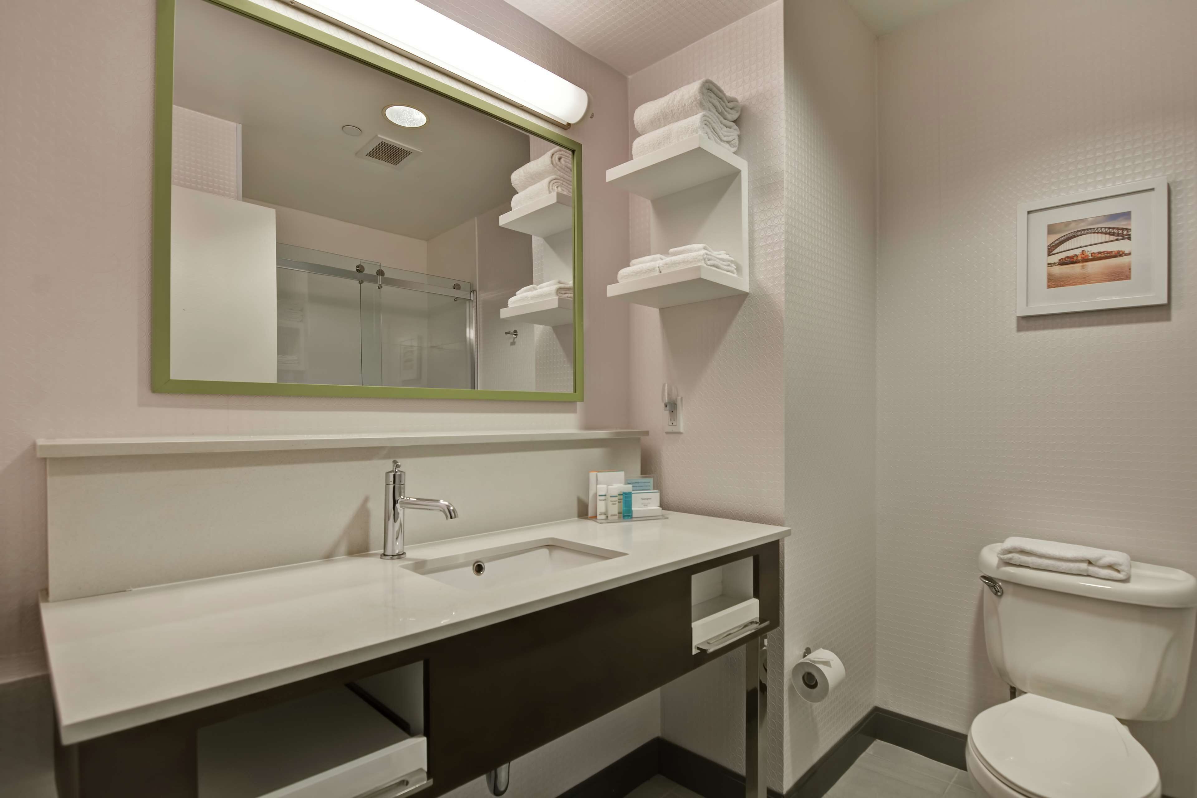 A bathroom with a sink, mirror, toilet, and towel storage.