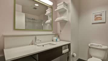 A bathroom with a sink, mirror, toilet, and towel storage.