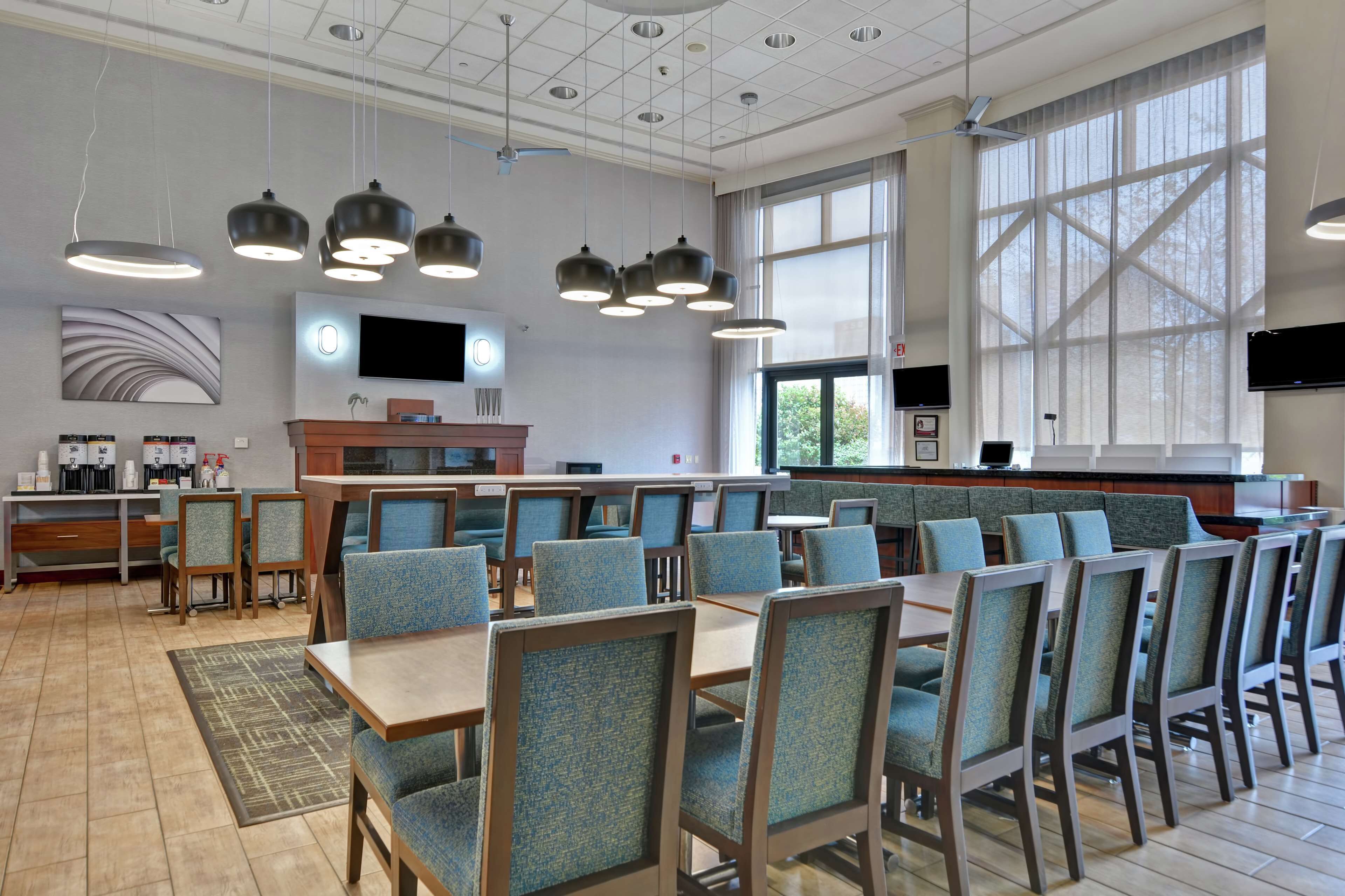 A spacious dining area with multiple tables and chairs, a coffee station, and large windows providing natural light.