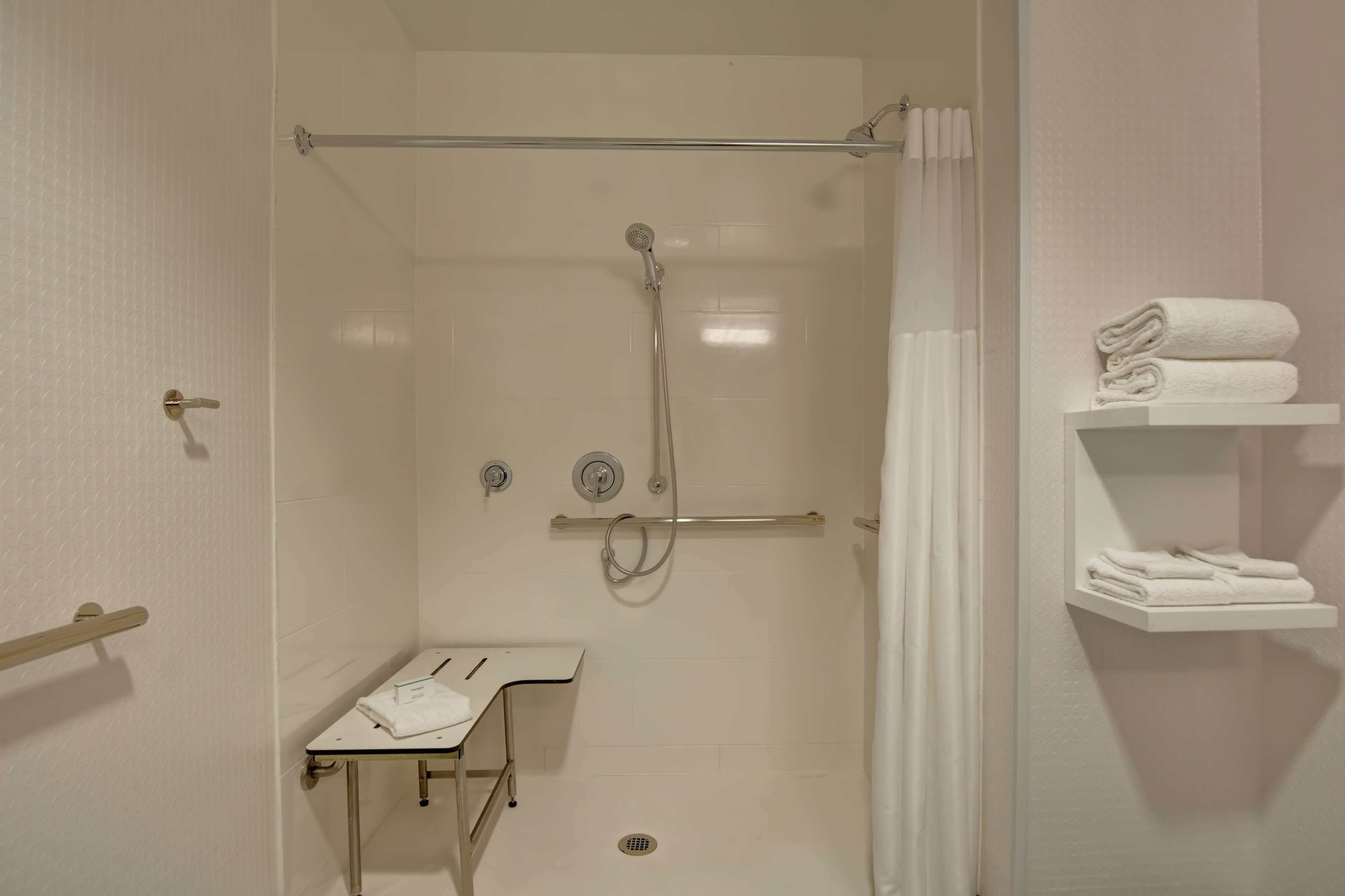 Une douche à l’italienne avec une porte en verre, un porte-serviettes et une petite table sur laquelle est posée une serviette.