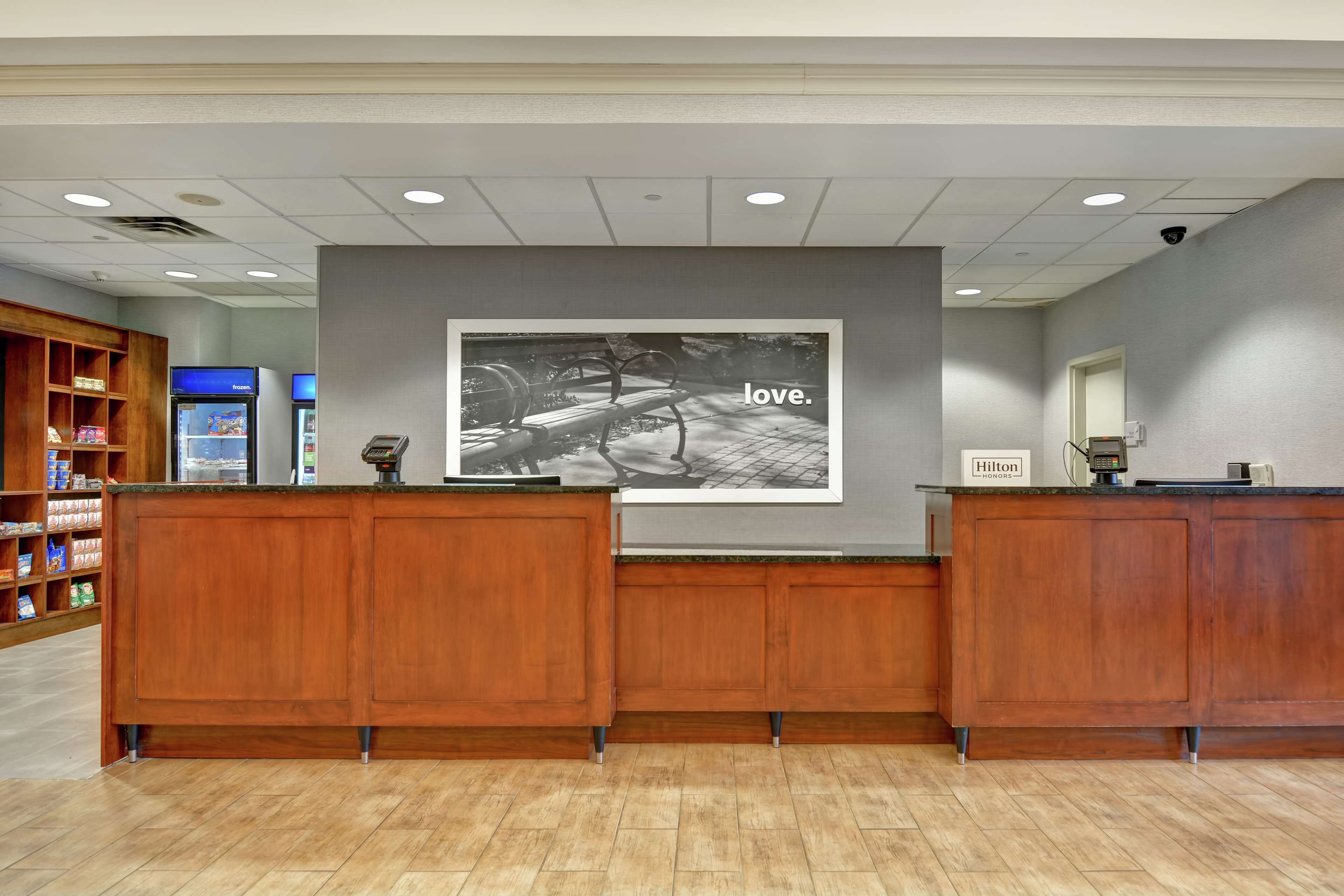 A reception area with wooden reception desks, a large framed photograph on the wall, and a minibar refrigerator.