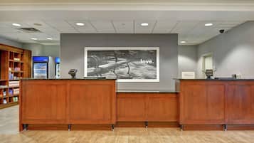 A reception area with wooden reception desks, a large framed photograph on the wall, and a minibar refrigerator.