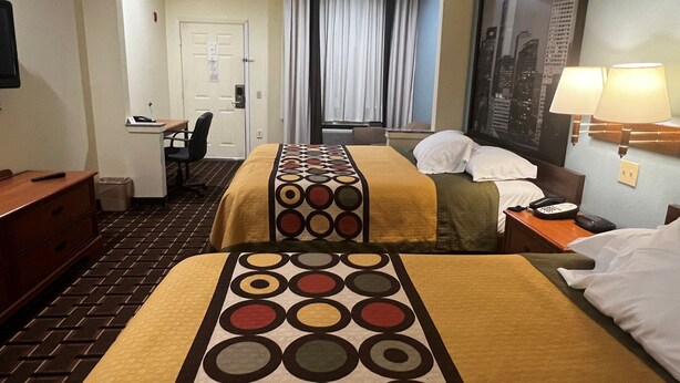 Habitación de hotel con dos camas, un escritorio, una silla, una lámpara y una ventana con cortinas.