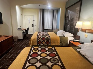 Habitación de hotel con dos camas, un escritorio, una silla, una lámpara y una ventana con cortinas.