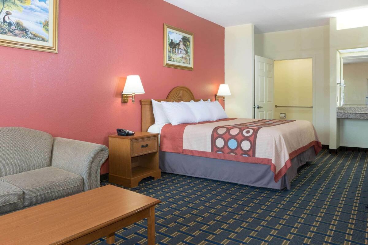 A hotel room with a bed, bedside tables, a sofa, and a small table.
