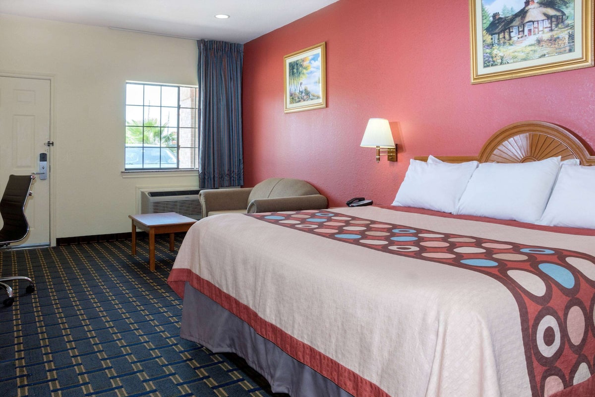 A hotel room with a large bed, a desk, a chair, a window, and a door.