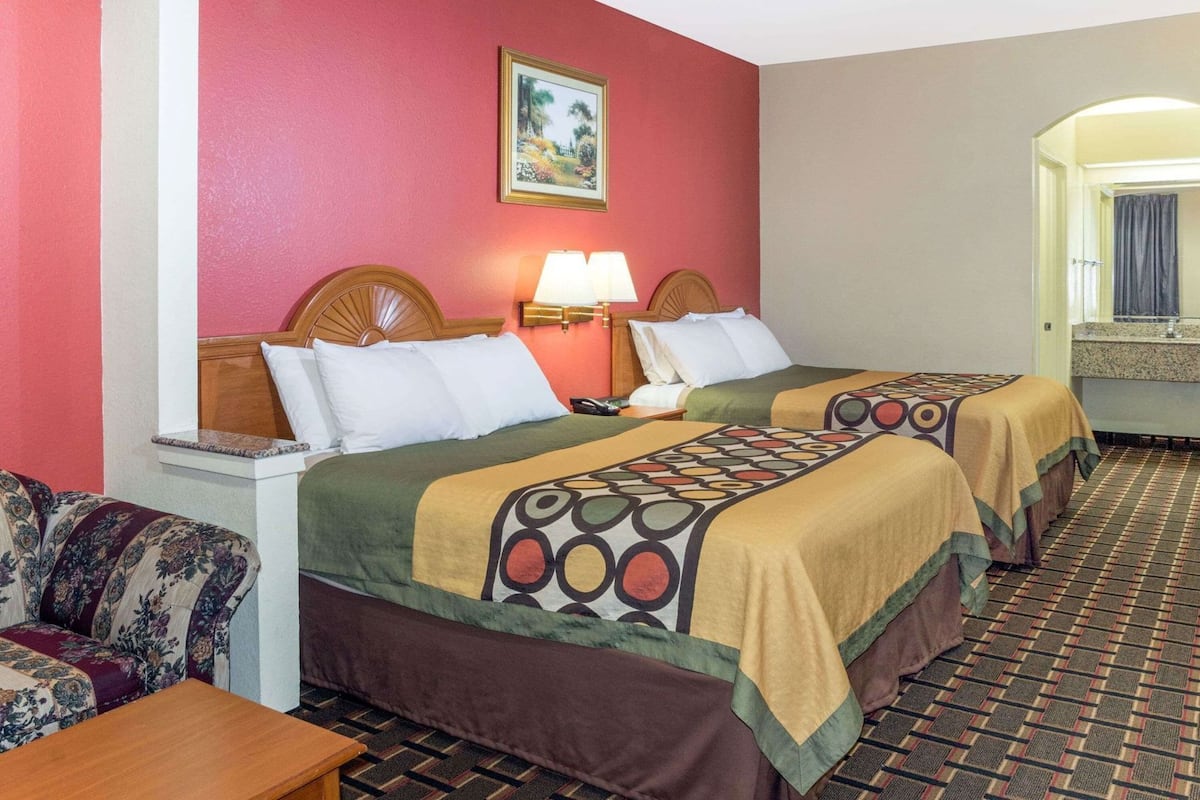 A hotel room with two beds, a sofa, a table, a lamp, and a painting on the wall.