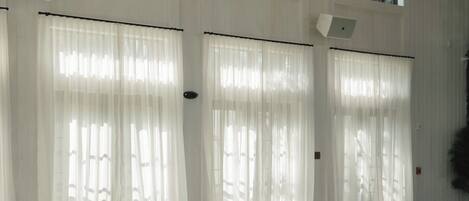 Una habitación amplia con ventanas grandes, cortinas blancas y colchonetas de ejercicio con equipo de fitness.