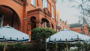 Een gebouw van rode baksteen met gebogen ramen en een balkon. Op de voorgrond staan witte parasols met blauwe accenten.