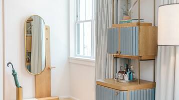 Una habitación con un tocador de madera, un espejo, un estante con libros y objetos decorativos, y una ventana con cortinas.