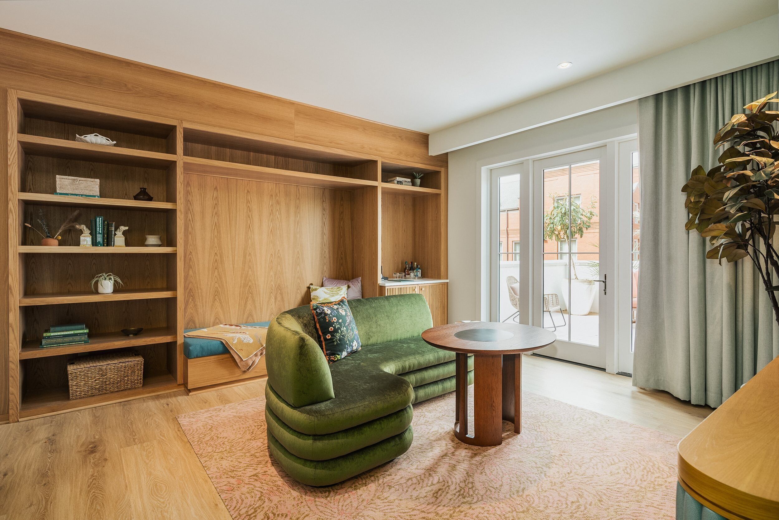 A modern living room with a green sofa, wooden shelving, and a dining table.