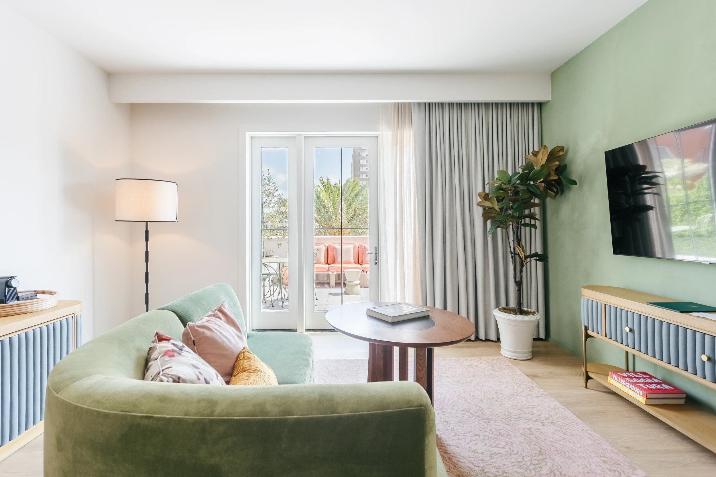 Una sala de estar moderna con un sofá verde, una mesa de centro, un televisor y un balcón con mobiliario exterior.