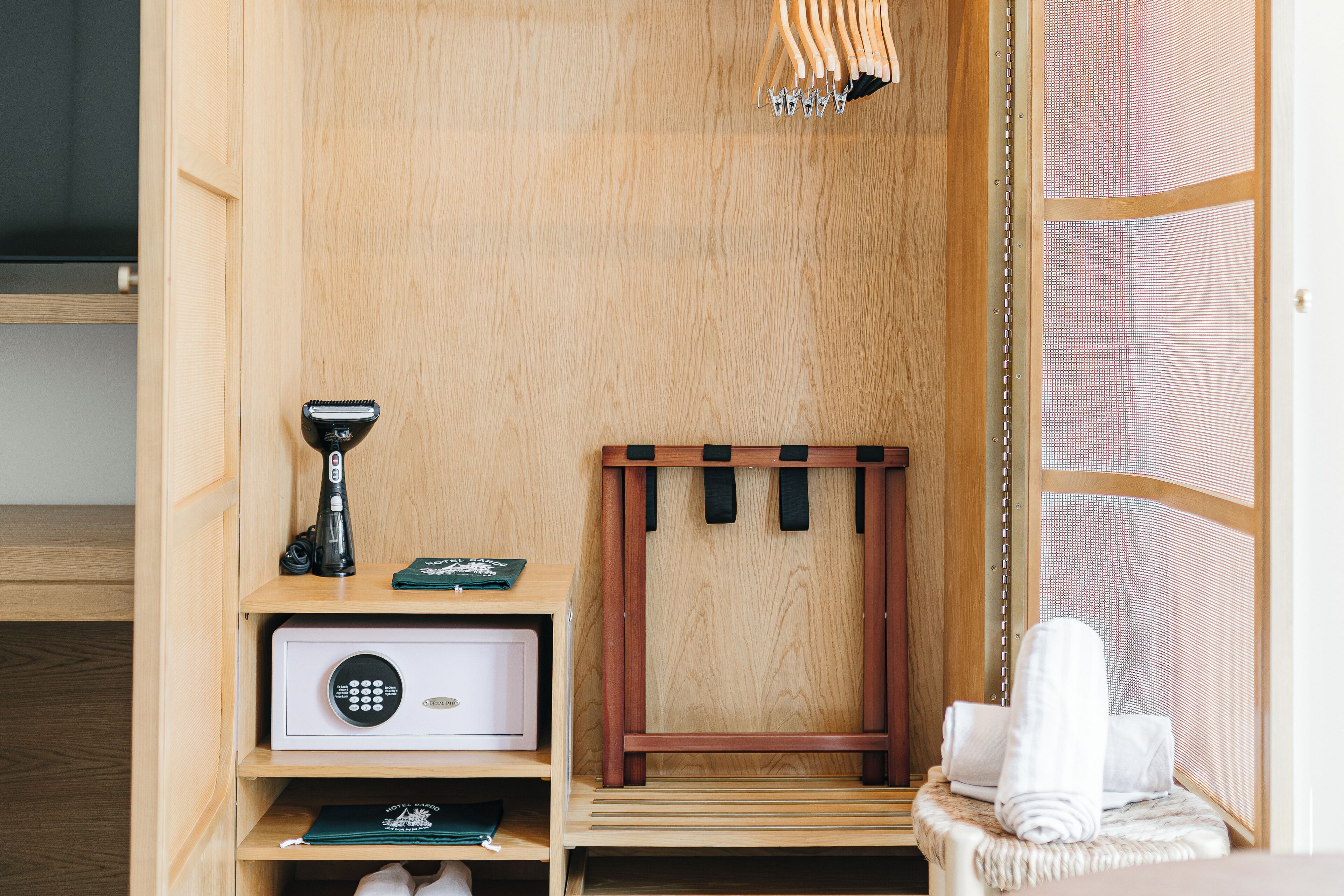 A wooden closet with a hanging rack, a safe, and a towel on a bench.