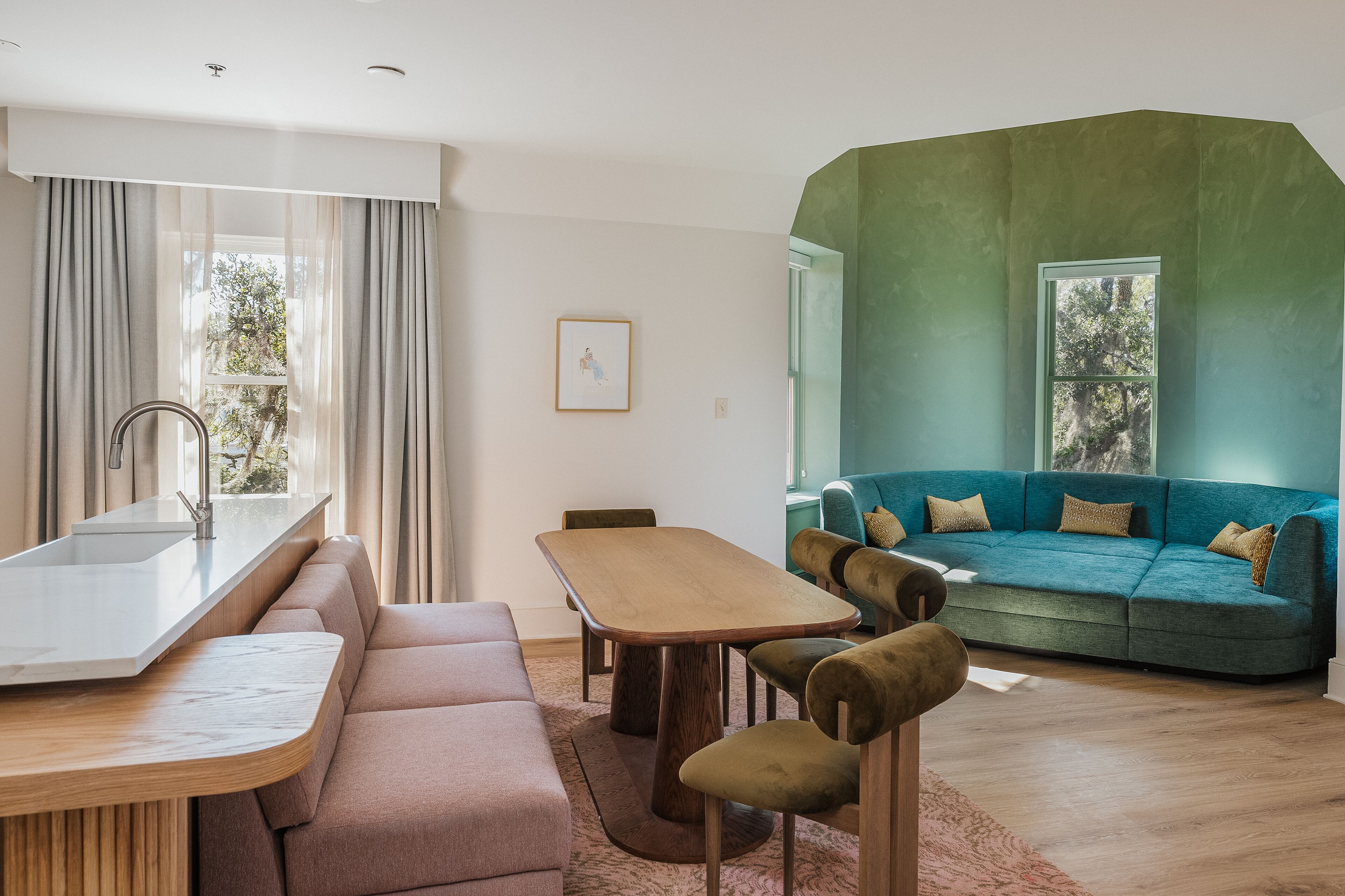 A modern living room with a kitchen area, a teal sofa, and a wooden dining table.