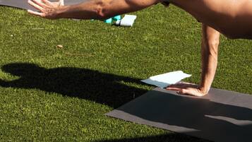 A yoga class on an outdoor grassy area with exercise mats and a large planter in the background.