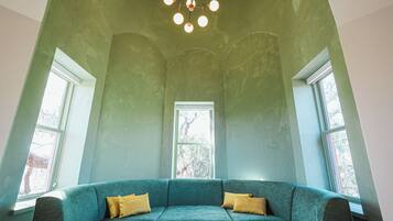 A room with a teal sofa, two windows, and a ceiling light fixture.