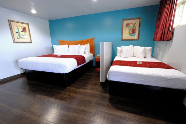 A hotel room with two beds, a wooden floor, and artwork on the walls.