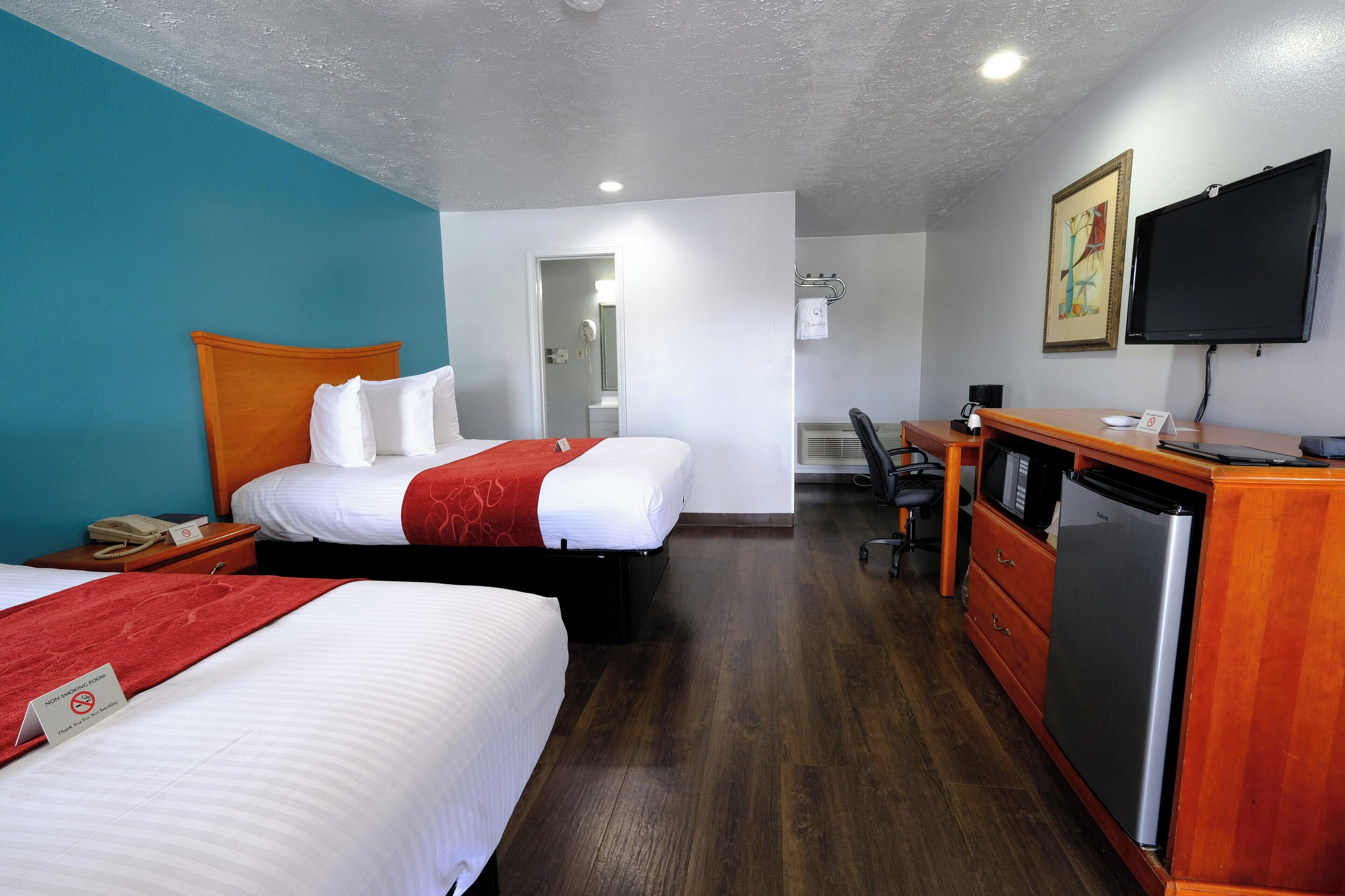 Quarto de hotel com duas camas, uma escrivaninha, televisão e frigorífico.