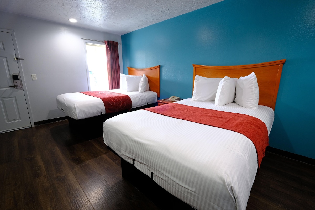 Habitación de hotel con dos camas, piso de madera y una pared de acento azul.