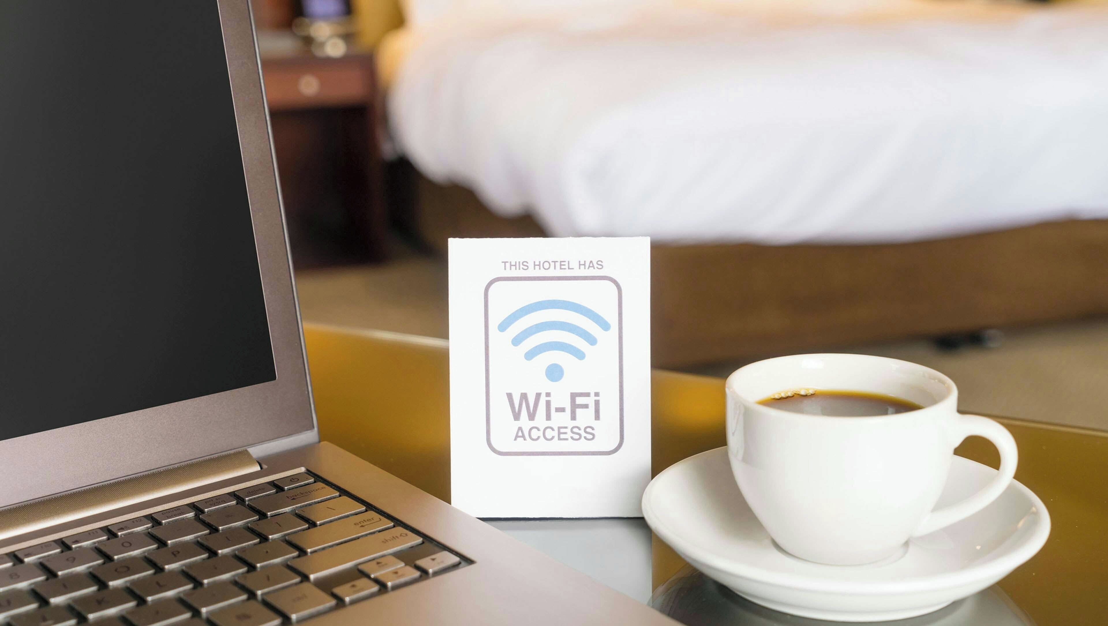 Ein Laptop, ein Schild für WLAN und eine Tasse Kaffee auf einem Tisch im Hotel.
