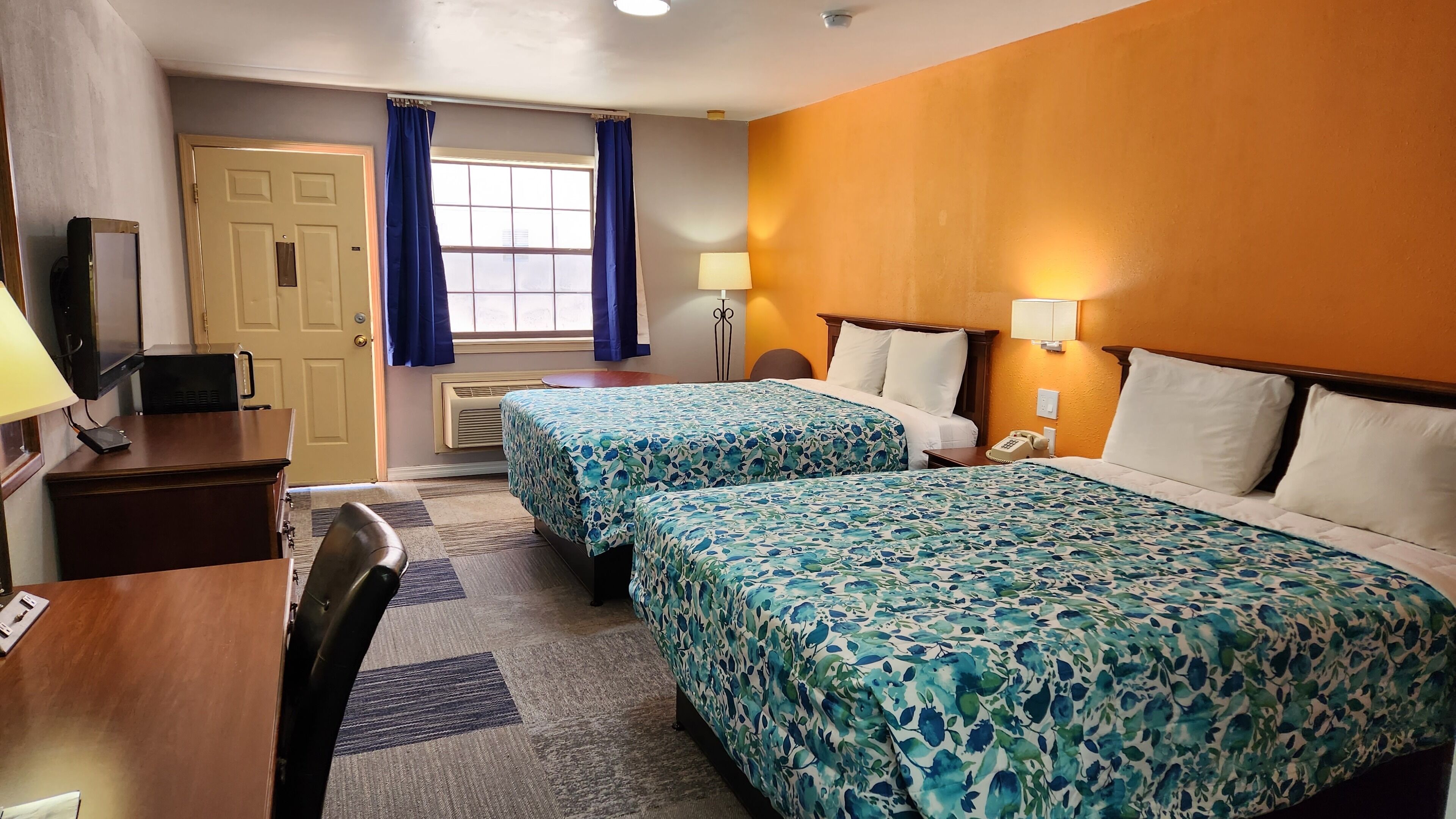 A hotel room with two beds, a desk with a computer, a lamp, and a phone.
