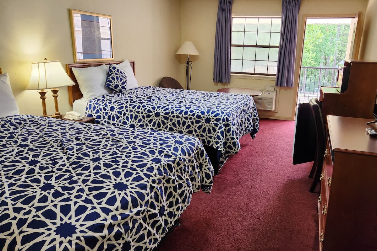 A hotel room with two beds, a desk with a computer, a lamp, and a window with curtains.