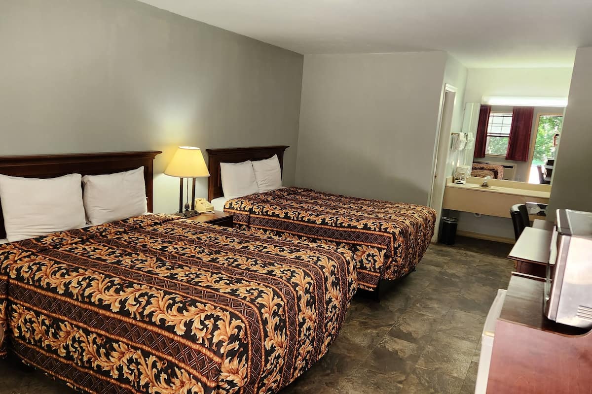 A hotel room with two beds, a desk, a chair, and a window with a view of trees.
