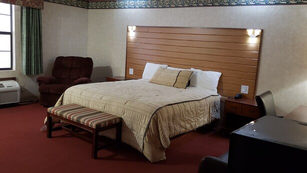 Una habitación de hotel con cama, una silla, un escritorio y una ventana con cortinas.