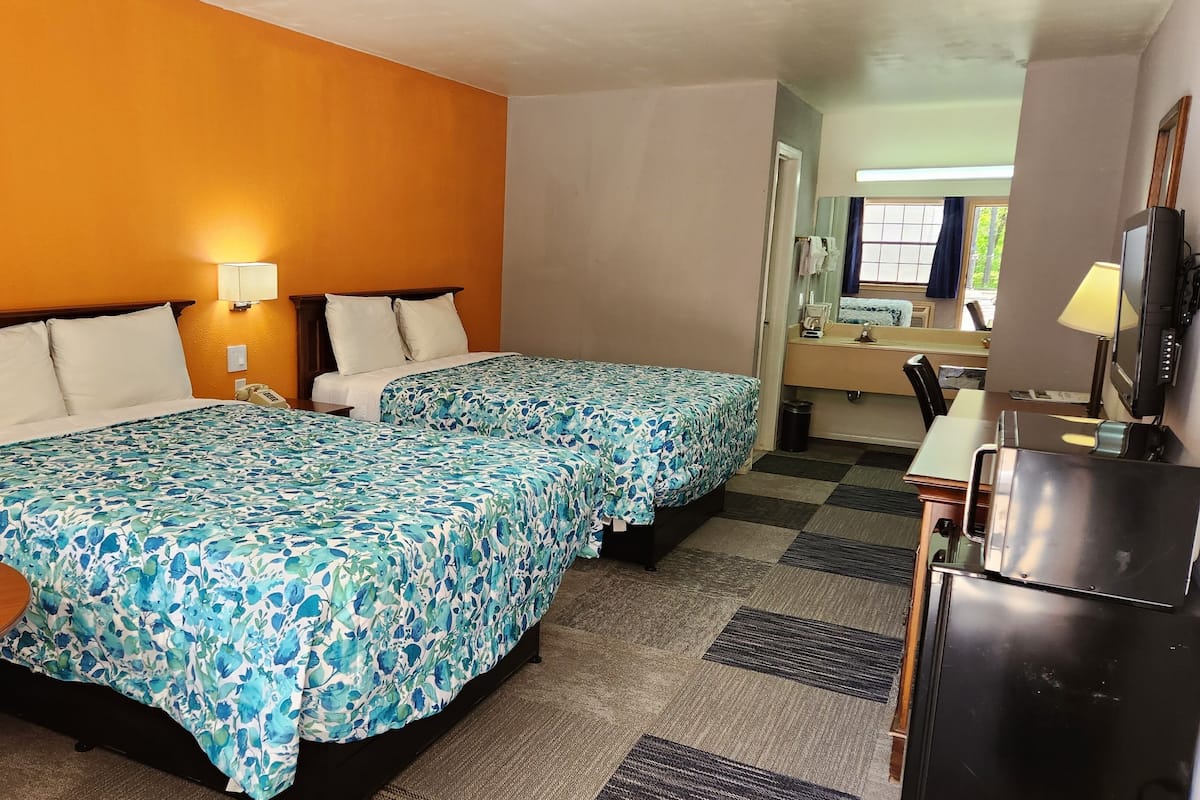 A hotel room with two beds, a desk, a TV, and a bathroom visible through an open door.