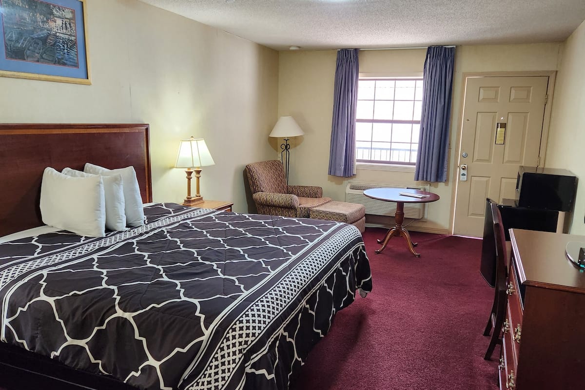 A hotel room with a large bed, a chair, a small table, a TV, and a door.