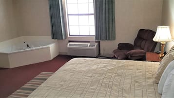 A hotel room with a large bed, a bathtub, a chair, a desk, a lamp, and a window with curtains.