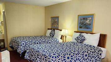 A hotel room with two beds, a desk, a chair, a lamp, and two framed pictures on the wall.