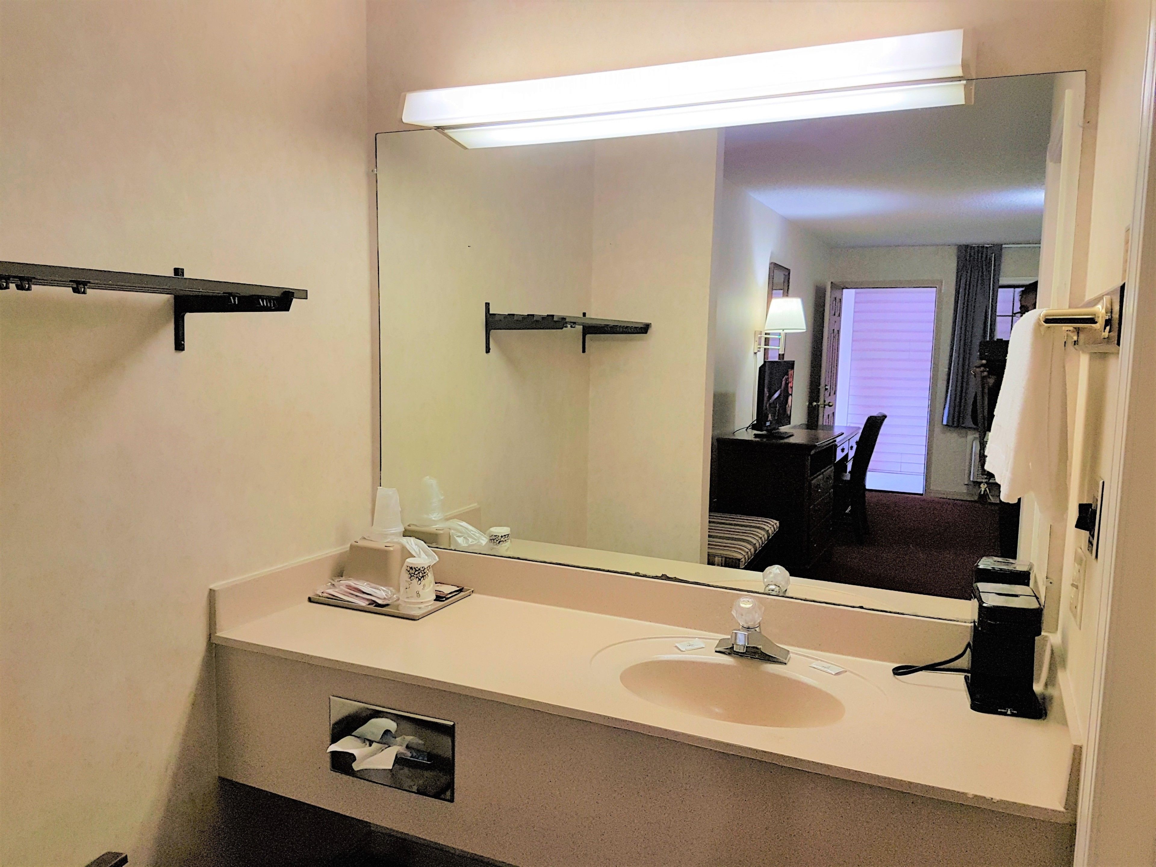 Un baño de hotel con un espejo grande, un lavamanos, un perchero para toallas y una cafetera.