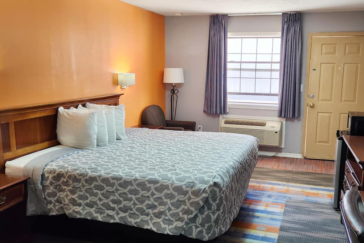 A hotel room with a bed, bedside tables, a desk, a chair, a TV, and a window with curtains.