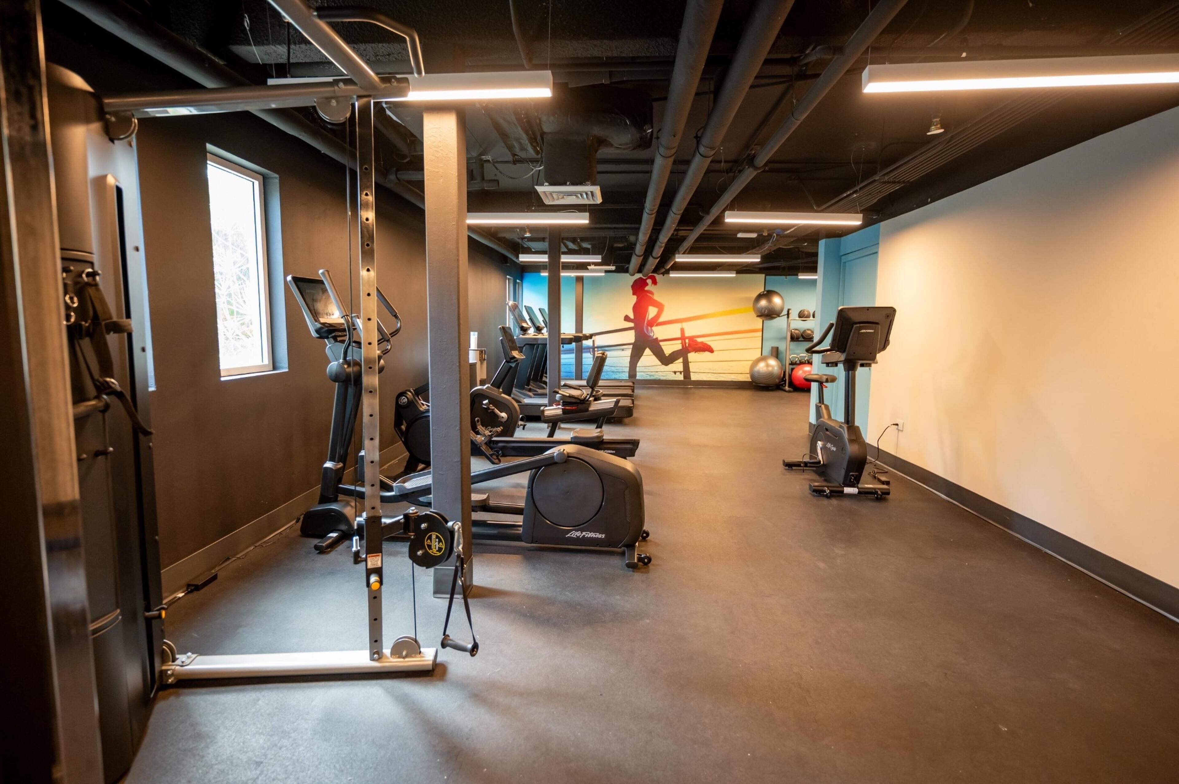 A gym with exercise equipment, a treadmill, and a wall with a silhouette of a person running.