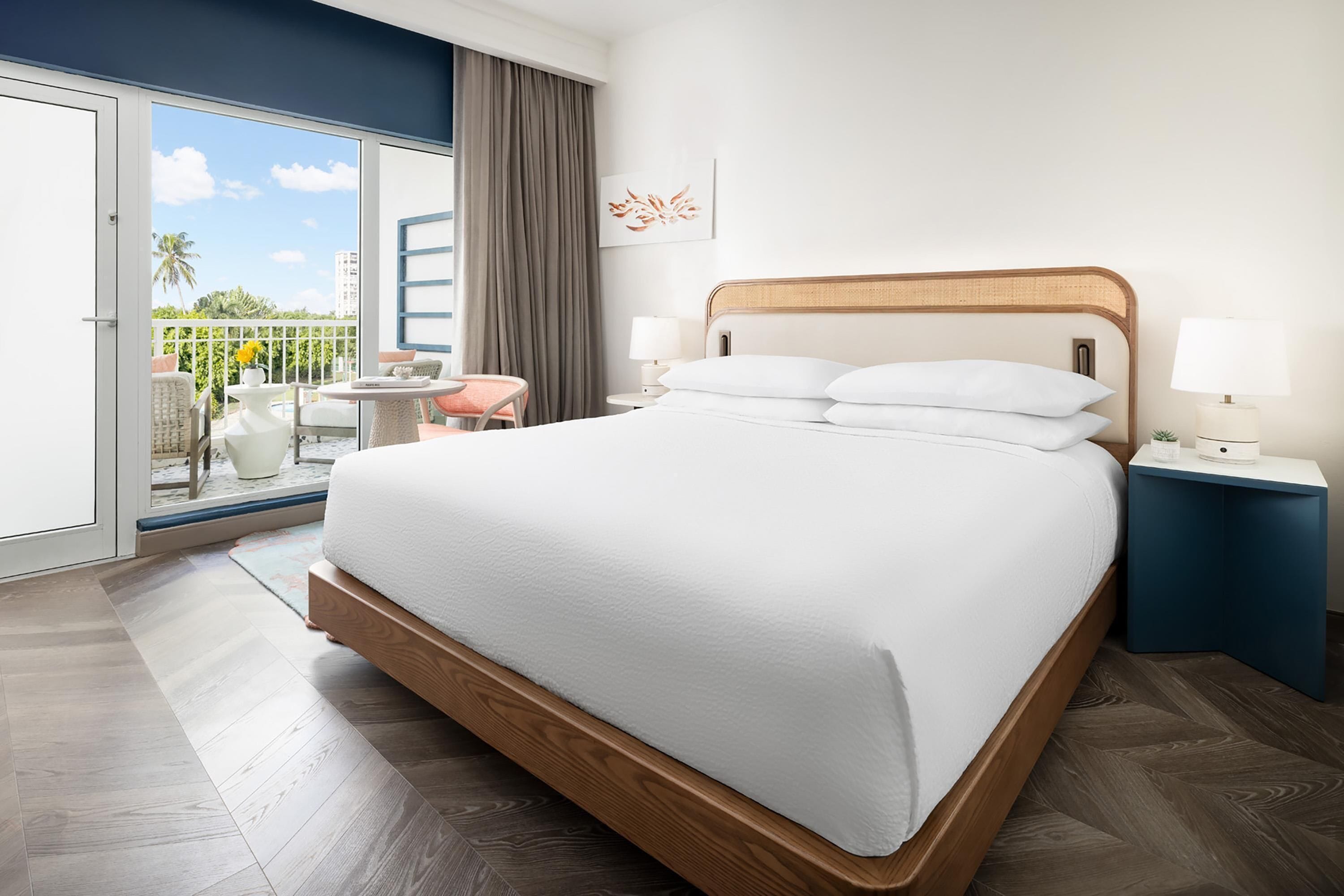 A hotel room with a large bed, a balcony with a view, and a small seating area.